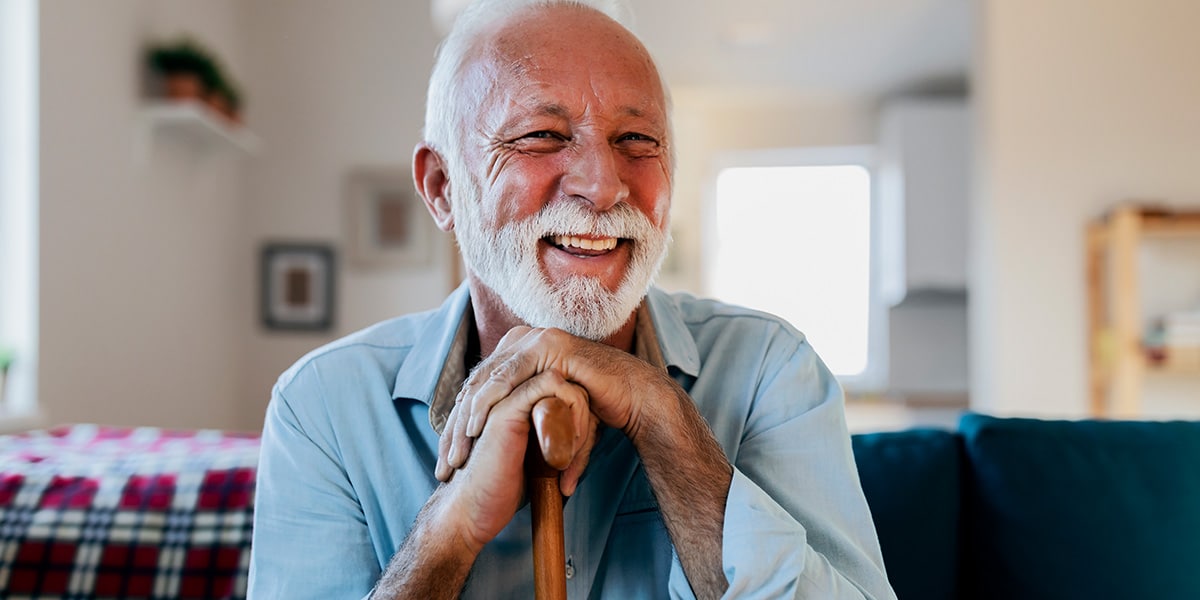 elderly man leaning on his walking stick and smiling